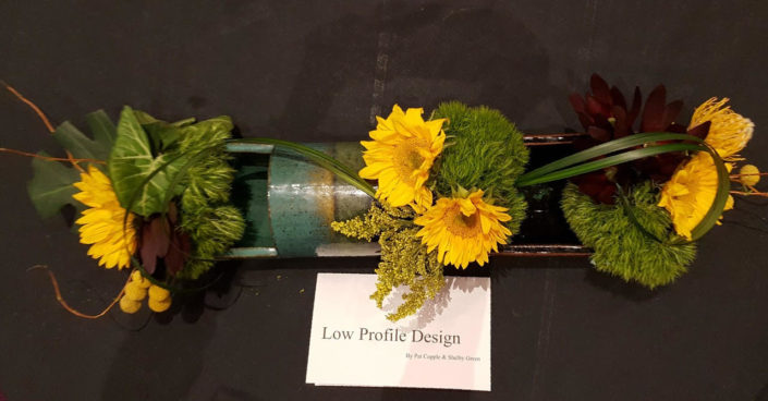 Horizontal shaped ceramic holds bright sunflowers and green accents.
